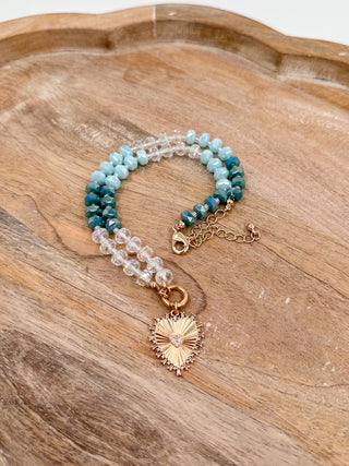 Beaded necklace with teal and light blue beads, crystal accents, and gold sunburst charm