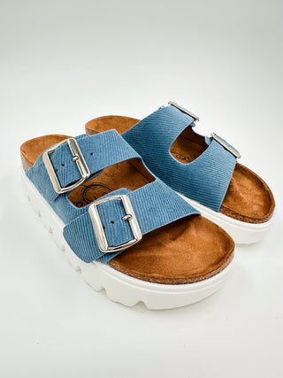 Faux suede slide sandals with two blue buckle straps and white platform sole