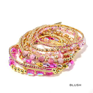 Blush pink beaded bracelet stack with gold-tone chains, round charms, and rhinestones