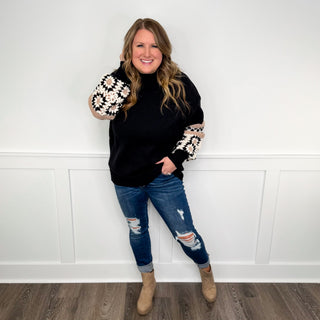 Women's outfit: black sweater with embroidered cuffs, blue distressed jeans, tan ankle boots