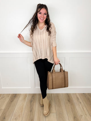 Beige V-neck tunic top, black leggings, tan ankle boots; holding tan tote bag.