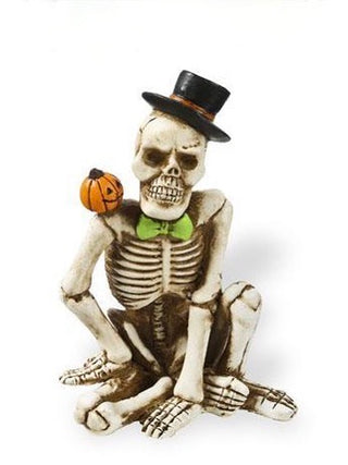 Skeleton resin decor figure with black hat, green scarf, and pumpkin treat