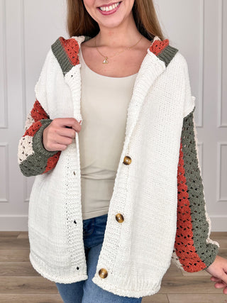 Cream hooded knit cardigan with long sleeves, patchwork red and gray, button front