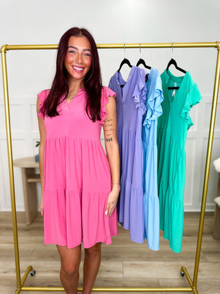 Woman in a pink dress standing next to a rack of colorful dresses.