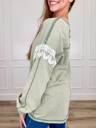 Sage green knit long-sleeve top with V-neck and white lace detail on sleeve cuffs