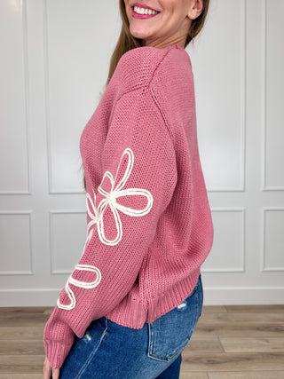 Pink knit sweater side view with white bow embroidery on sleeve and ribbed cuffs