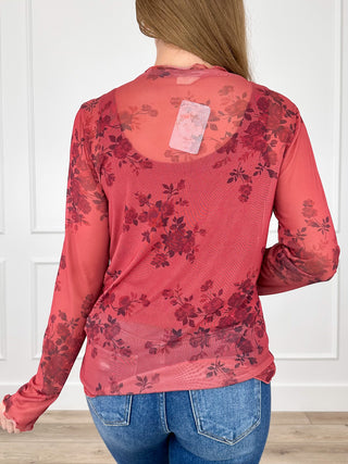Back of red sheer mesh long-sleeve top with dark floral print and small tag label