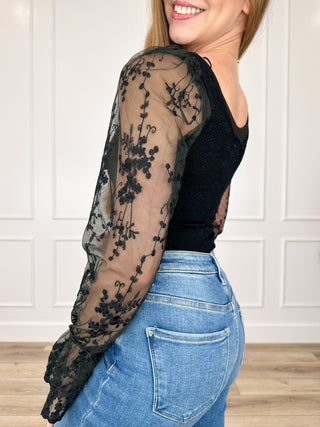 Black fitted bodysuit with sheer floral mesh long sleeves and scoop neckline