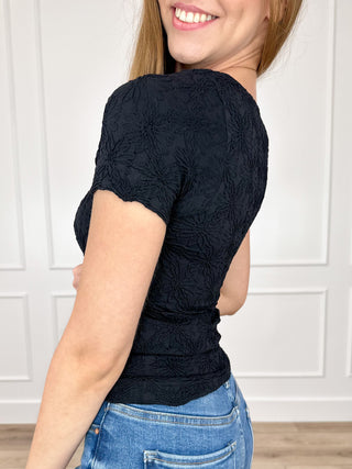 Black short-sleeve top with textured floral pattern and ruched waist