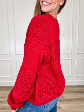Red knit long-sleeve sweater, side view with relaxed sleeves and cuffs.