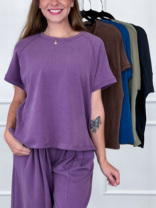 Purple short-sleeve crewneck top with relaxed draped fit and curved hem