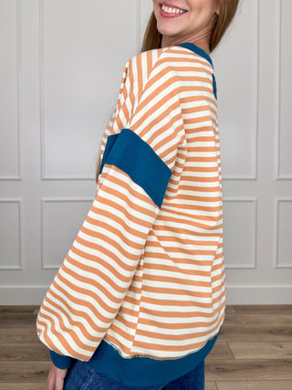 Striped knit long-sleeve top, side view, orange/white stripes with teal trim