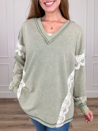 Sage green knit long-sleeve top with V-neck and white lace trim at cuffs and hem