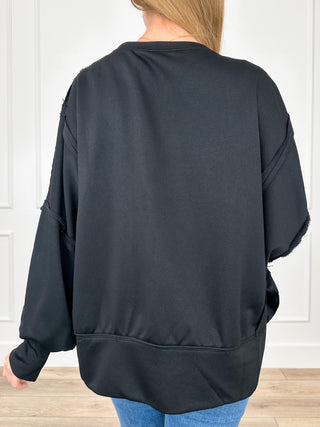 Black long-sleeve top back view with dropped sleeves and rounded hem.