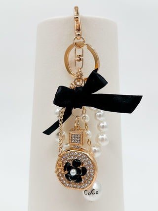 Gold round charm keychain with rhinestones, black flower, CoCo detail, and pearl dangles