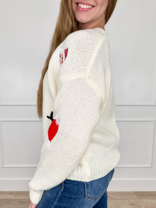 Cream knit cardigan with long sleeves, button front, and festive patch on sleeve