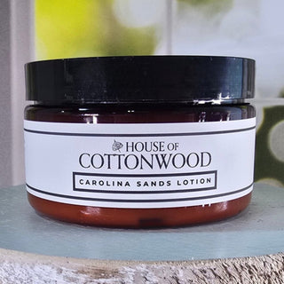 Jar of 'Carolina Sands Lotion' from 'House of Cottonwood' on a wooden surface.