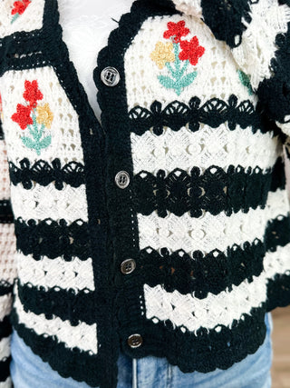 Button-front cardigan close-up: cream knit with black trim and red floral stripe panels