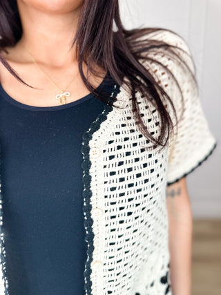 Cream open knit cropped cardigan front with scalloped dark edging and button placket detail