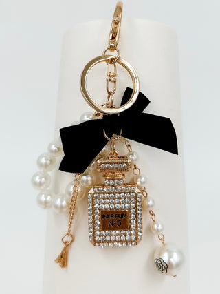 Gold perfume keychain with rhinestone bottle charm, black ribbon, and pearl dangles