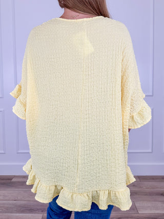 Lightweight short sleeve V-neck top in pale yellow, back view with ruffled hem