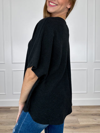 Black knit short-sleeve top, side view with relaxed shoulder and curved hem