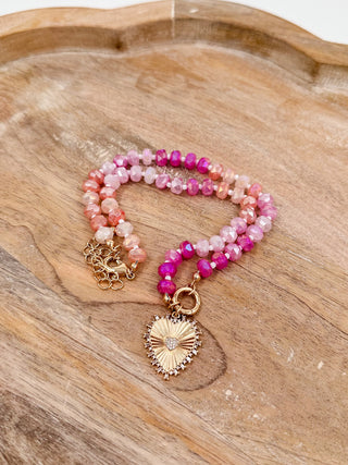 Beaded necklace with pink and magenta beads, crystal accents, and gold sunburst charm