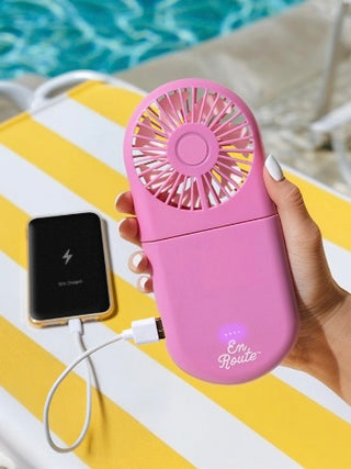 Pink power bank fan held in hand with connected charging cables.