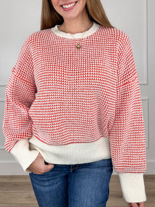 Red-and-white knit long-sleeve sweater with ribbed cuffs and hem, small button neckline.
