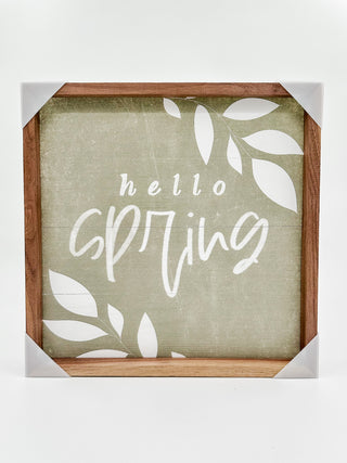 Wood spring sign with 'hello spring' script and leaf accents on green background