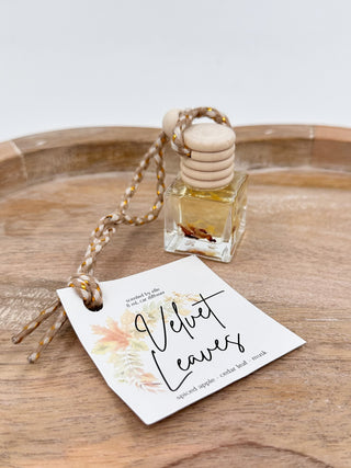Clear glass scent diffuser bottle with cork cap and braided cord, labeled “Velvet Leaves”.