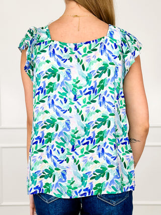Rayon blend cap-sleeve top in blue and green leaf print, rounded back yoke