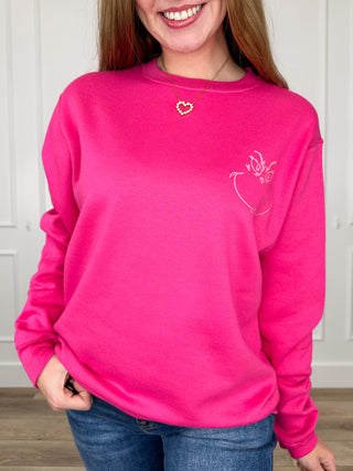 Pink crewneck sweatshirt with small heart and reindeer graphic on the chest.