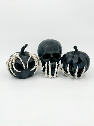 Three black pumpkin skeleton decorations with skull faces and bone hands