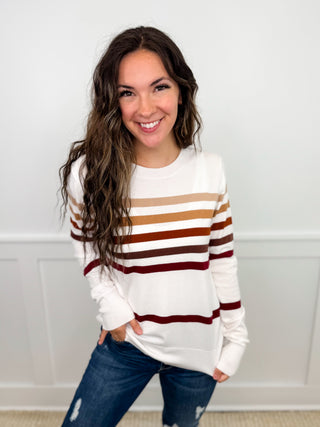 White knit long-sleeve sweater with tan and rust stripe bands and ribbed cuffs