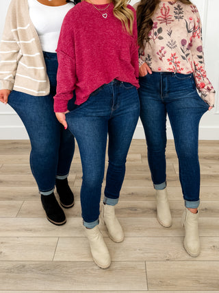 Three women standing together wearing dark blue jeans, styled with different tops and ankle boots on a light wood floor.