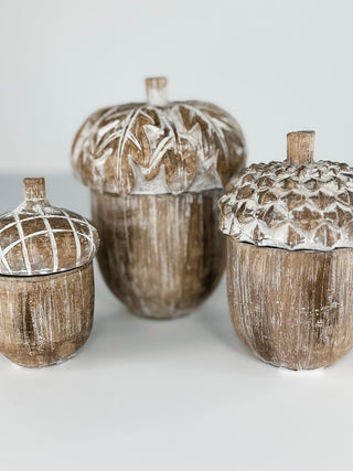 Three rustic acorn-shaped decorative containers with textured brown and white distressed finishes, arranged on a light gray surface against a neutral background.