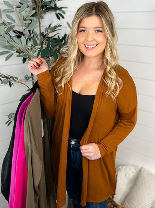 A woman wearing a brown cardigan holding a handful of other colors of the sweater.