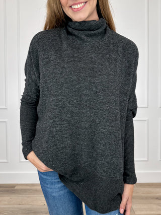 Dark charcoal knit turtleneck top with long dolman sleeves, draped asymmetrical hem