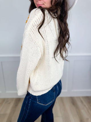 Cream knit long-sleeve cardigan, side view with sunflower detail on sleeve