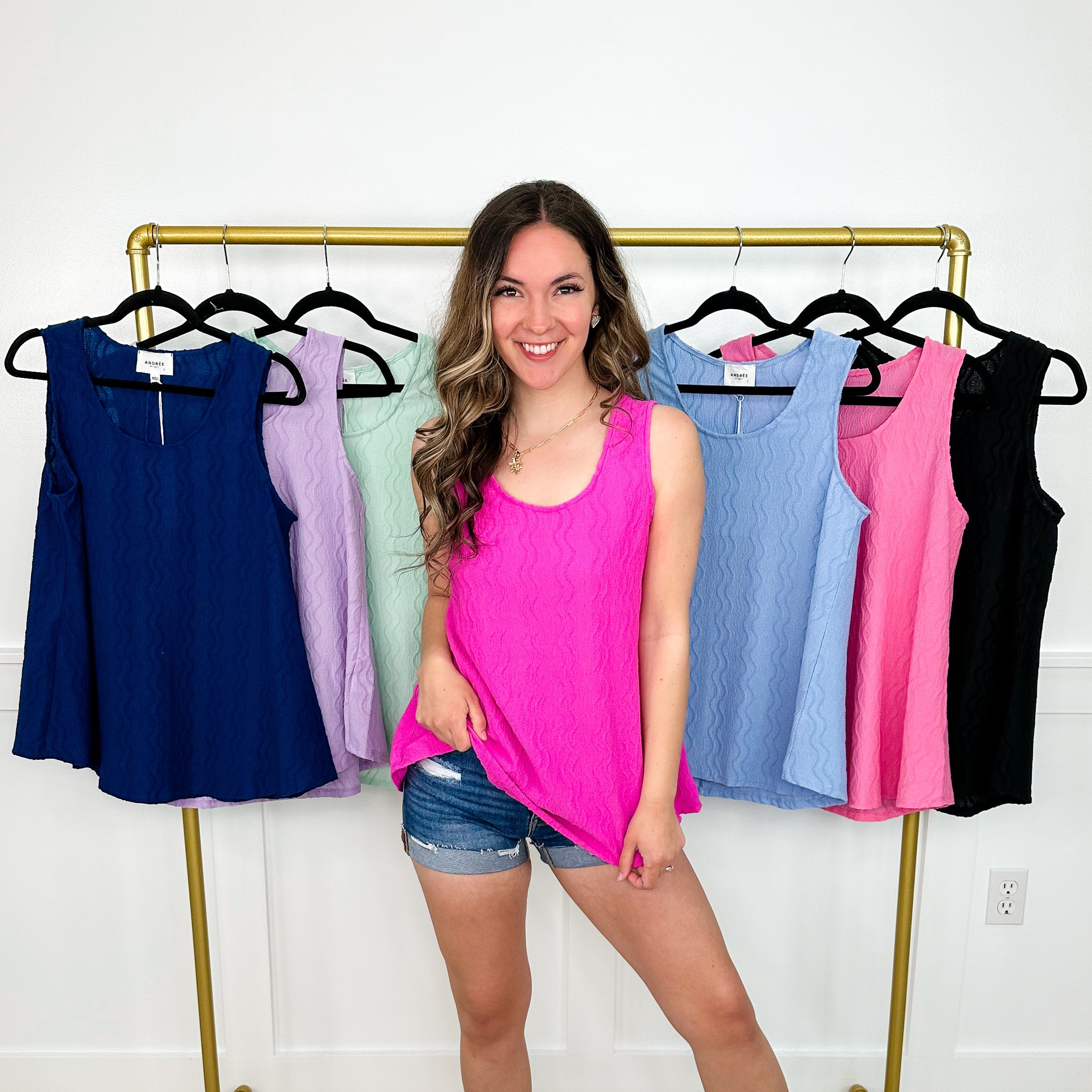 Woman standing in front of a clothing rack with various colored tank tops.