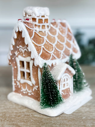 Light-up gingerbread cottage shelf sitter with white icing details and miniature evergreen trees