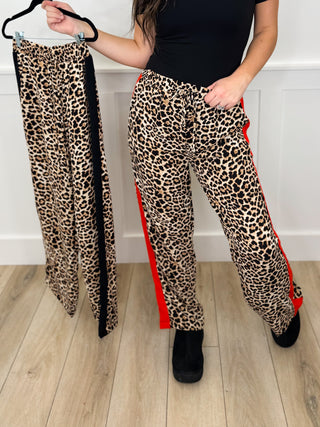 Leopard print pants with red side stripe, one worn and one held up for view