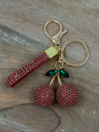 Gold keychain with red rhinestone cherry charms and green leaf accents.