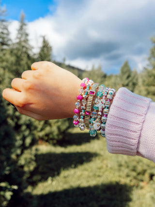 Multi-strand beaded charm bracelets stack on wrist with pink and turquoise accents