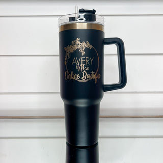 Black gold-accent tumbler with clear lid, side handle, and front logo.