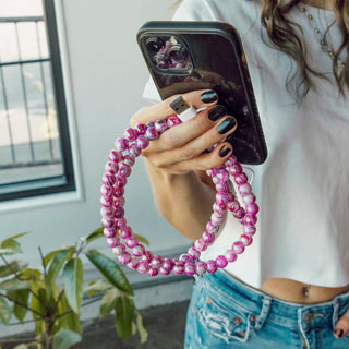 Marble pink beaded phone charger wrapped around a phone, USB plug connected