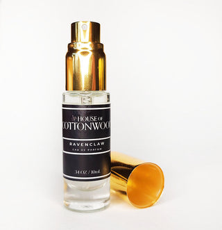 A travel-sized bottle of Ravenclaw Eau De Parfum by House of Cottonwood, with a gold-colored cap and label, displayed next to a gold-colored object, possibly a spray nozzle.