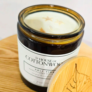 Candle in a glass jar labeled 'House of Cottonwood' on a bamboo surface.