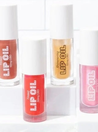 Set of tinted CBD lip oils with assorted red, brown, gold, and pink bottles and caps